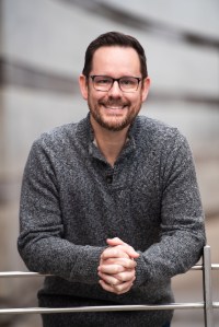 Dan, the Reading Dad, is leaning against a metal fence, hands clasped, smiling at the camera.